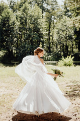 Fototapeta premium the bride in a white dress stands with her back to us and holds a bouquet of flowers