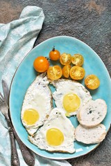  fried eggs and yellow cherry tomatoes. on a blue plate. yellow and blue. top view