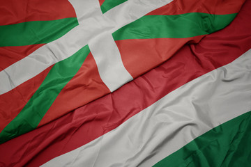 waving colorful flag of hungary and national flag of basque country.