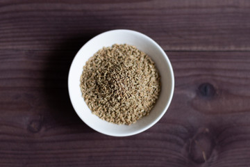 Ajowan seeds in white bowl on brown wooden background, top view