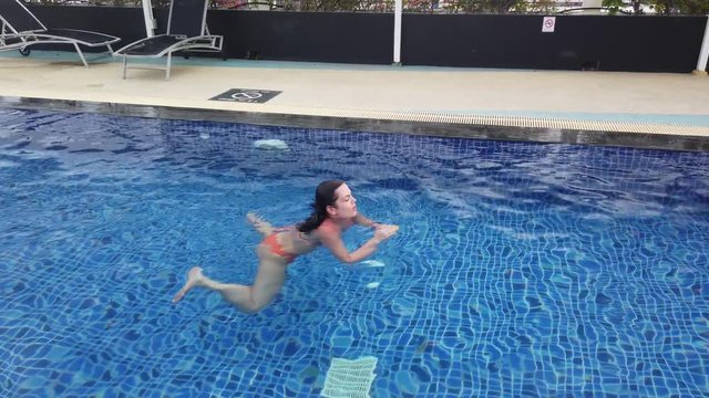 Beautiful girl in orange swimsuit swims in blue pool