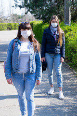 Two girls in medical masks walk along the road