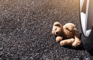 Lonely teddy bear with sad face lying next to the tyre, Brown bear falling down next to wheel with...