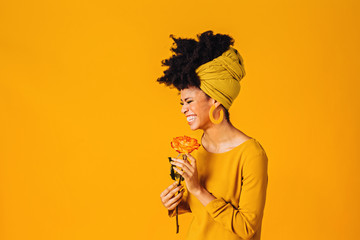 Profile portrait of a happy young woman holding yellow orange rose laughing, isolated on yellow background © Carlos David