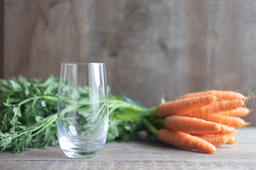 An empty glass on a wooden table and next to a bunch of carrots with green tops. Place for text