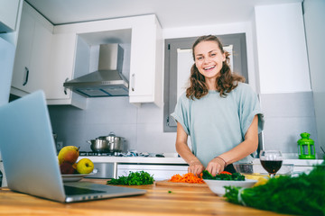 Laptop on kitchen table and cooking girl. cutting vegetables, online lesson, communication education, cooking, lifestyle concept