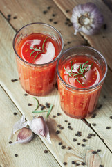 Tomato sauce in glasses garnished with fresh rosemary, garlic and black pepper on wooden table, overhead view, closeup, vertical, organic food concept
