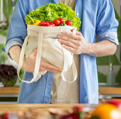 Young man holds whole shopping bag of vegetables