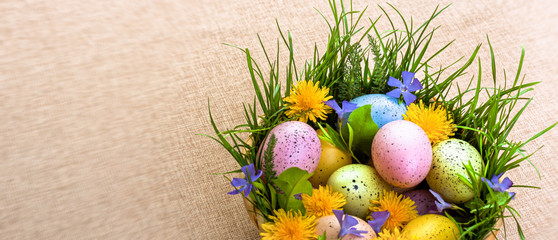 Easter. Congratulations on the spring holiday of Easter. Colorful eggs in a basket decorated with flowers and grass.