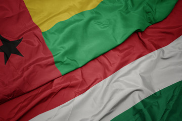 waving colorful flag of hungary and national flag of guinea bissau.
