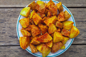 Tapa de Patatas bravas o patatas gajo en un plato blanco sobre mesa de madera.