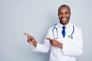 Photo of doctor dark skin guy family doc direct finger empty space advising epidemic rules steps disinfection safety wear lab coat neck tie stethoscope isolated grey color background