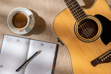 Coronavirus, Covid-19, workplace of a musician isolated at home, Guitar, coffee and pencil on blank...