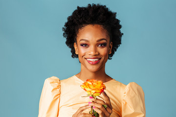 Profile portrait of a happy young woman holding yellow orange rose and smiling, isolated on blue background © Carlos David