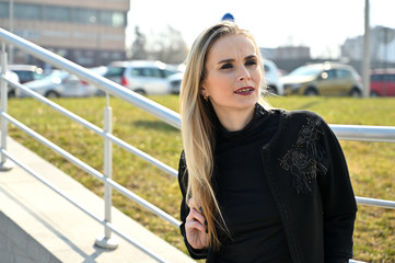 Model on the background of the railing of the stairs. Portrait of a young blonde Caucasian woman in the city outdoors on a sunny day.