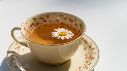 Ceramic teacup with tea and chrysanthemum inside on floral pattern saucer