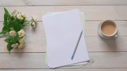 Top view: paper, blue pencil, a bunch of flowers and a cup of coffee on a wooden table