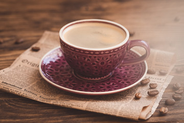 Cup of coffee with beans on newspaper background, business breakfast concept, selective focus, toned vintage