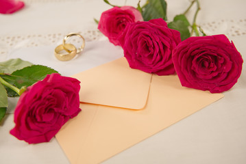 red rose flowers, rings, and an envelope on white desktop, copy space