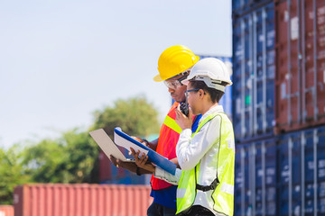 Worker man in hardhat and safety vest holding laptop and Female foreman talks on two-way radio control loading containers box from cargo