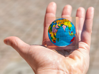 A male hand holds a colorful planet earth in the palm with a map in a transparent glass frame