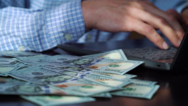 Hundred dollar bills falling on table of freelancer working on laptop