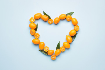 Heart made of tasty kumquat fruit on color background