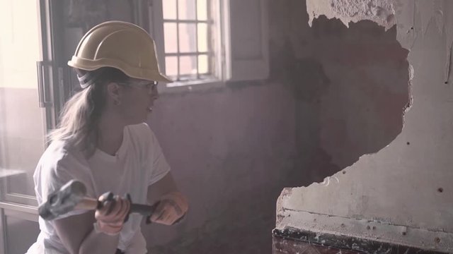 Slow motion video of a young tough construction worker woman wearing protective personal equipment successfully hitting and breaking a wall with a big hammer