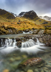 Fototapeta na wymiar Small Cascading Waterfall Stream At Deepdale Beck In The Lake District National Park With Snow On Mountain Peaks. 