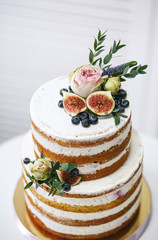High birthday cake, decorated with fruits and flowers. On a white background. The cream and sponge cake are visible in layers. Open cake.