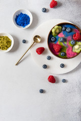 Healthy Breakfast Detox green, blue, pink spirulina Smoothie with Banana, topped with kiwi and berries in a Bowl on gray background. Vegan Meal. Top view, copy space