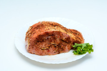 On a white background a piece of pork. The meat is seasoned with garlic, pepper, paprika and cooked for the oven. Nearby are green leaves of lettuce.. Concept - meat cooking