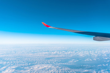 Naklejka na ściany i meble Airplane wing above beautiful blue cloudy sky in the morning (view from airplane)