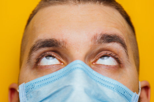 Closeup Portrait Of An Attractive Young Man Rolled His Eyes In A Protective Mask On His Face. Fear Of Getting Sick, Coronavirus Concept. Without Pupils.