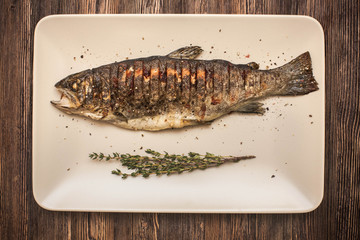 grilled trout on a wite plate with a bunch of thyme