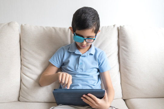 Portrait of boy in glasses with patch for glasses. Boy with tablet. Treat lazy eye, amblyopia, strabismus.  Remote learning. Distance education. Covid-19. Quarantine. Coronavirus. Homework.