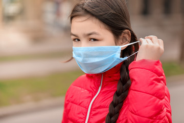 Little Asian girl wearing protective mask on city street. Concept of epidemic