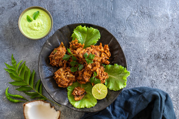 Indian cuisine. pakora traditional Indian deep-fried snack. pakoras on black plate with coconut chutney sauce curry leaves. national appetiser authentic vegetarian food. Asian travel food. top view.