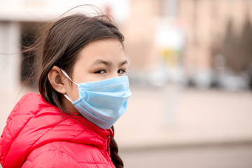 Little Asian girl wearing protective mask on city street. Concept of epidemic