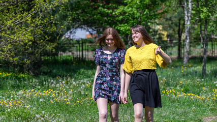 Fototapeta premium Young girls have fun time in the park. The sisters communicate and share secrets. Happy sisters are enjoying a warm spring day