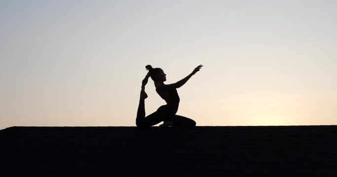 Silhouette of young woman doing acrobatics on the roof over sunset sky background in summer evening - video in slow motion