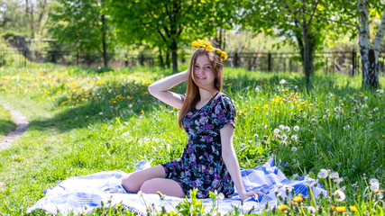 Beautiful and young girl resting on the nature. Wreath of yellow dandelion flowers on his head