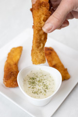 Hand dip fried chicken in dill sauce above white marble table background