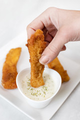 Hand dip fried chicken in dill sauce above white marble table background
