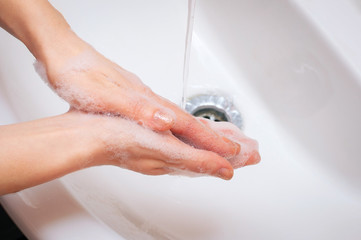 Young woman washing hands with soap over sink in bathroom. Palms togethertop view.