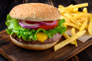 Burger with french fries on a wooden background. Beef burger with fresh lettuce, tomato and cheese.