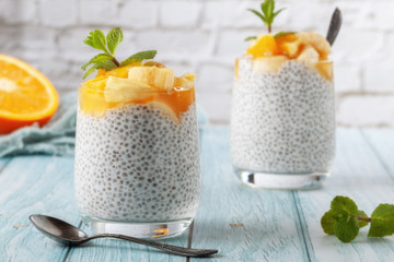 Fototapeta na wymiar Chia pudding with banana in two glass glasses with raw chia seeds on a blue wooden table
