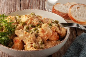 Chicken fillet with green peas stewed in a creamy sauce on a wooden table