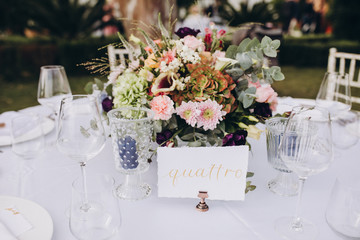 Wedding banquet. Tables in a green meadow are decorated with flower arrangements, on the tables are white tablecloths, plates with napkins, glasses and candles, cutlery. White bulbs hang over tables