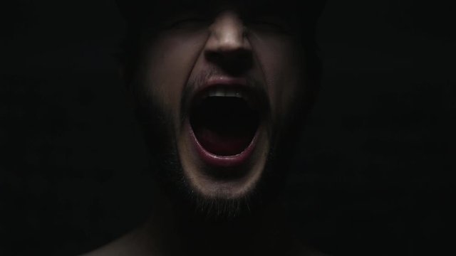 Dark close-up portrait of male mouth screaming on black background.